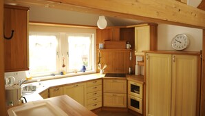 A kitchen with wooden cabinets, a sink, and a clock on the wall. - Exclusive vacation apartment | dream location at the foot of the Alps | suitable for allergy sufferers (Füssen)