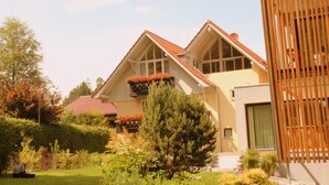 A two-story house with a sloped roof, large windows, and a garden with various plants and flowers. - Exclusive vacation apartment | dream location at the foot of the Alps | suitable for allergy sufferers (Füssen)