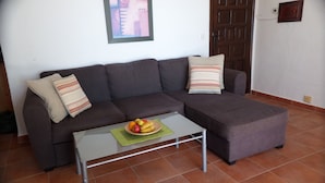 A living room with a brown sectional sofa, two striped pillows, a glass coffee table with a fruit bowl, and a framed picture on the wall. - Apartment in a beautiful, quiet location with stunning panoramic views across the sea (Velilla-Taramay)