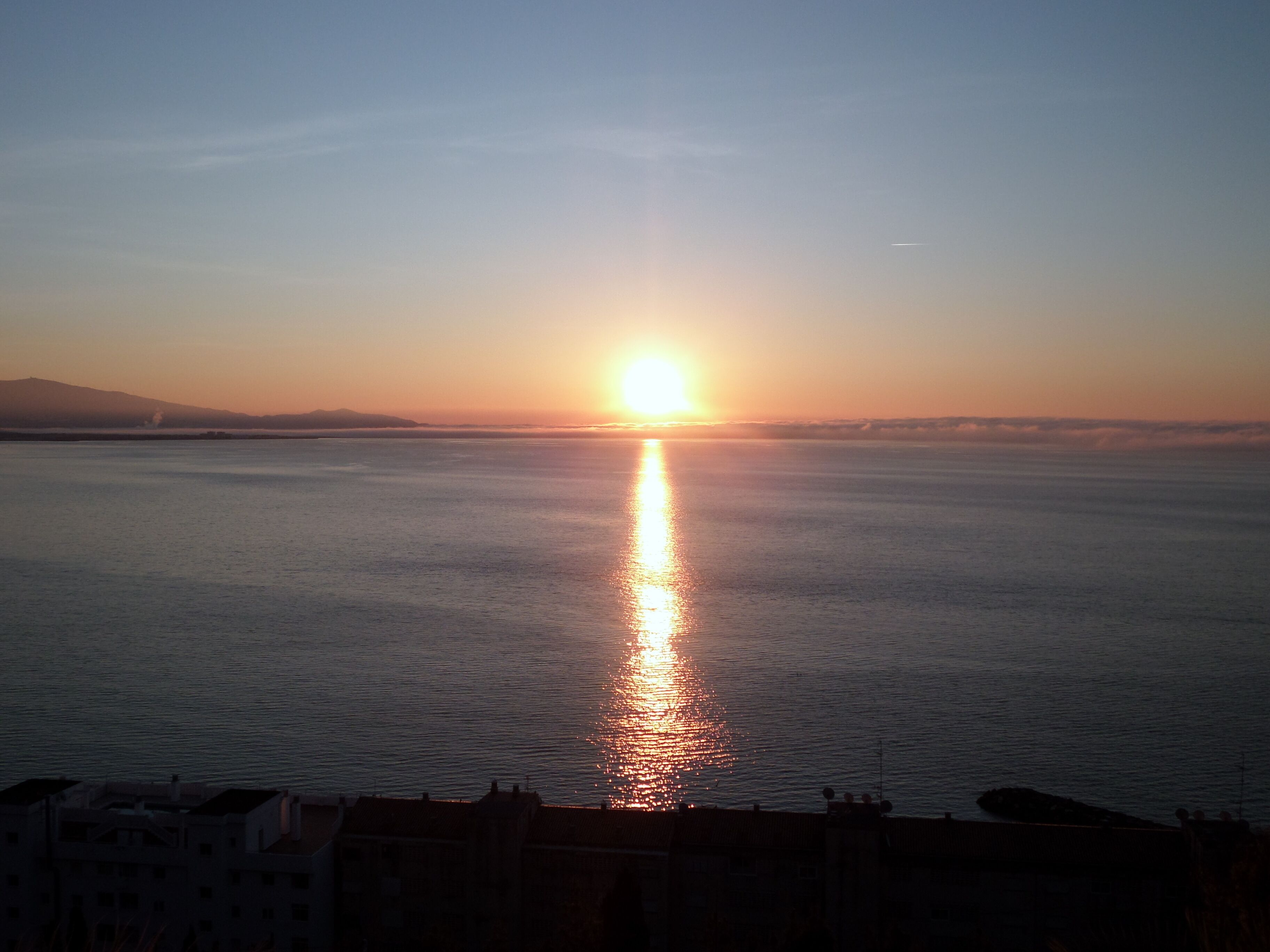 A sunset over a calm sea with a distant shoreline.