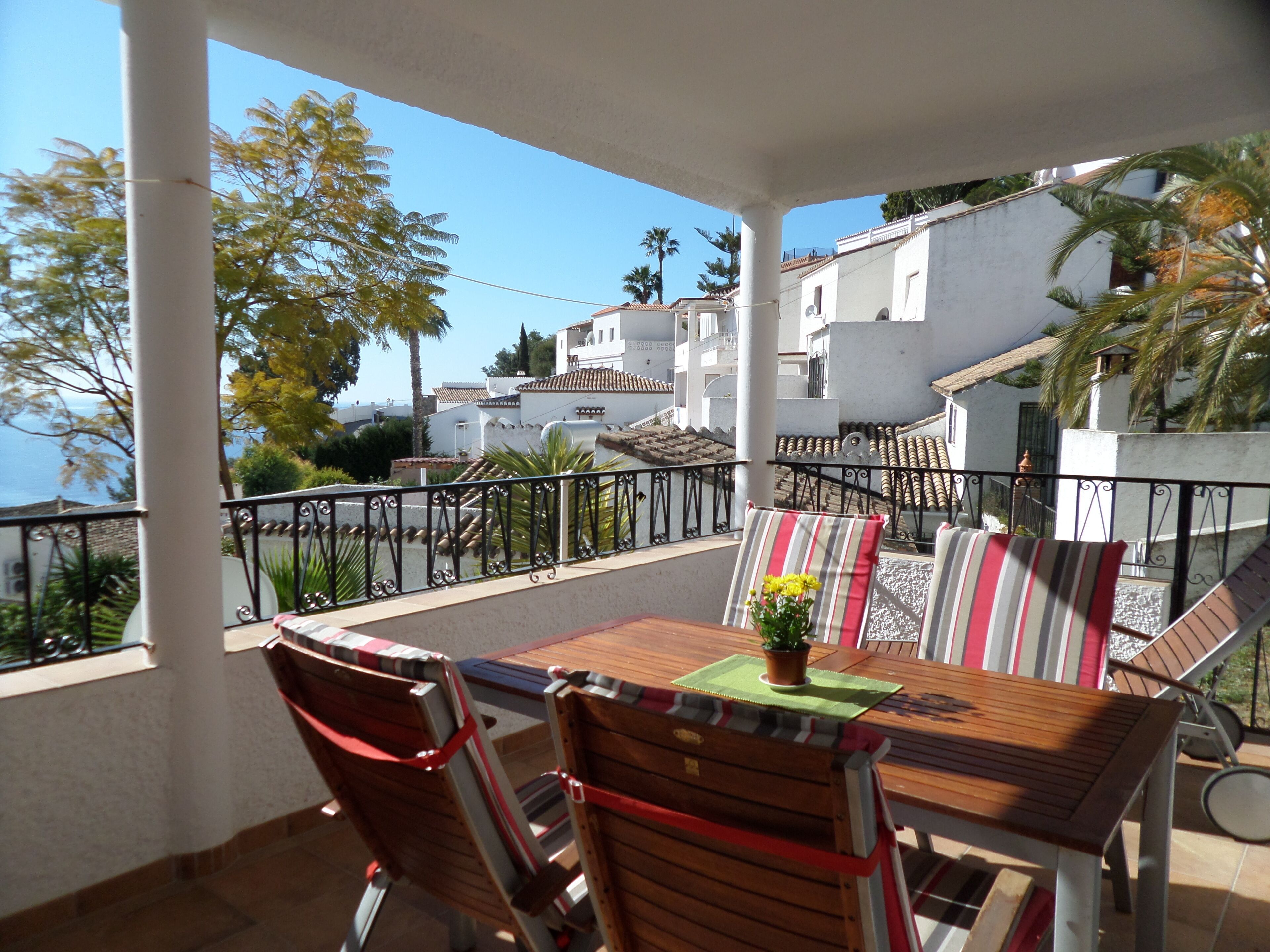 A terrace with a table, chairs, and a view of white buildings and palm trees.