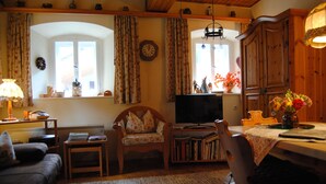 A cozy living room with a sofa, a wooden chair, a television, and a dining table with a vase of flowers. - Romantic holiday home (Dörflis)