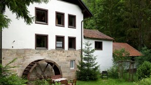 A white building with multiple windows and a stone water wheel. - Romantic holiday home (Dörflis)