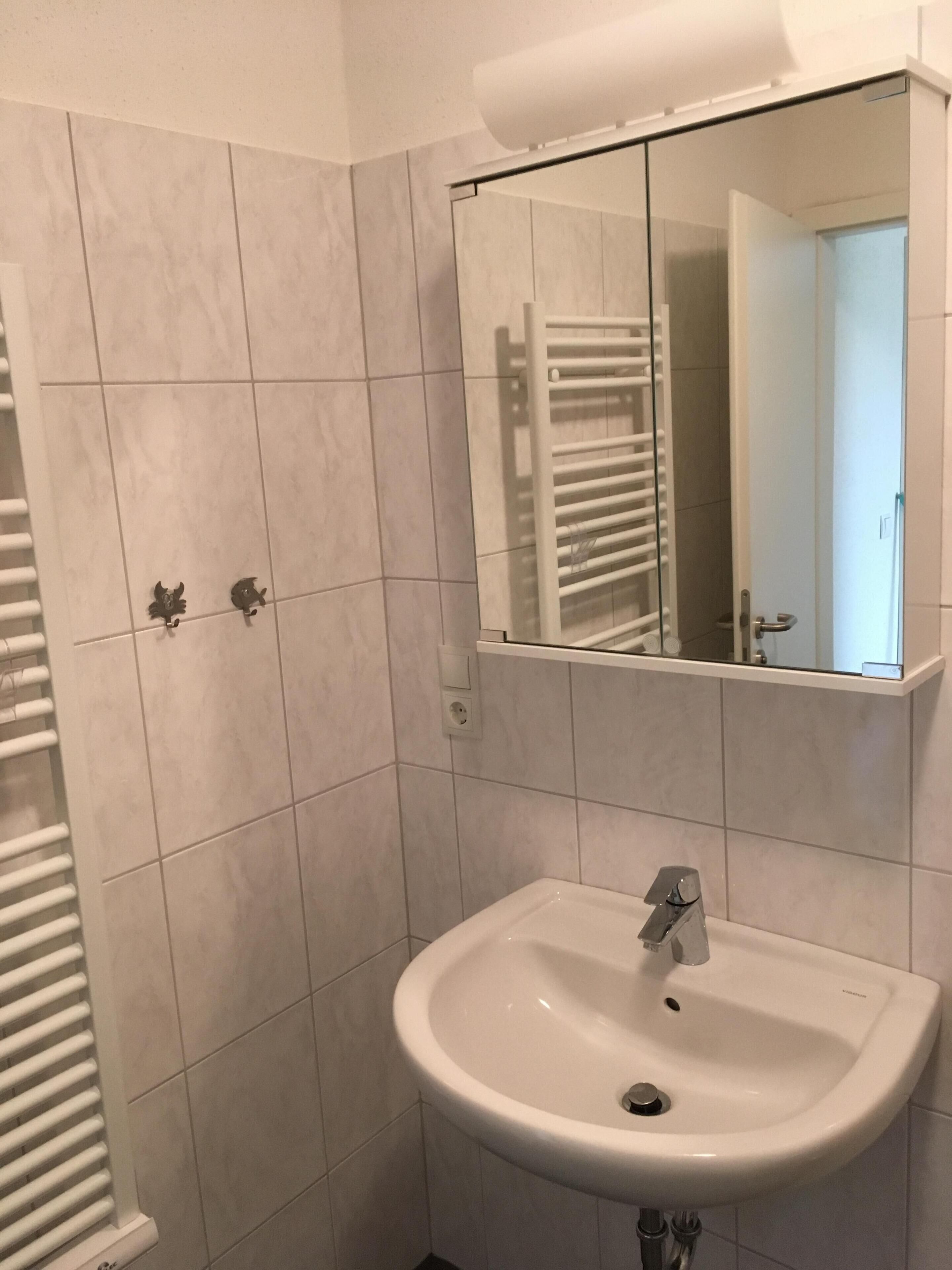 Ein Badezimmer mit einem weißen Waschbecken, einem Spiegel und einem Handtuchhalter.