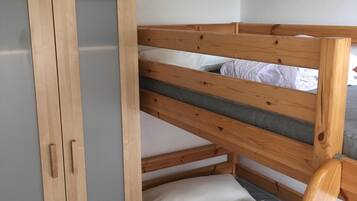 A bunk bed with a wooden frame and grey bedding, a wooden wardrobe with a mirrored door, and a plain white wall.