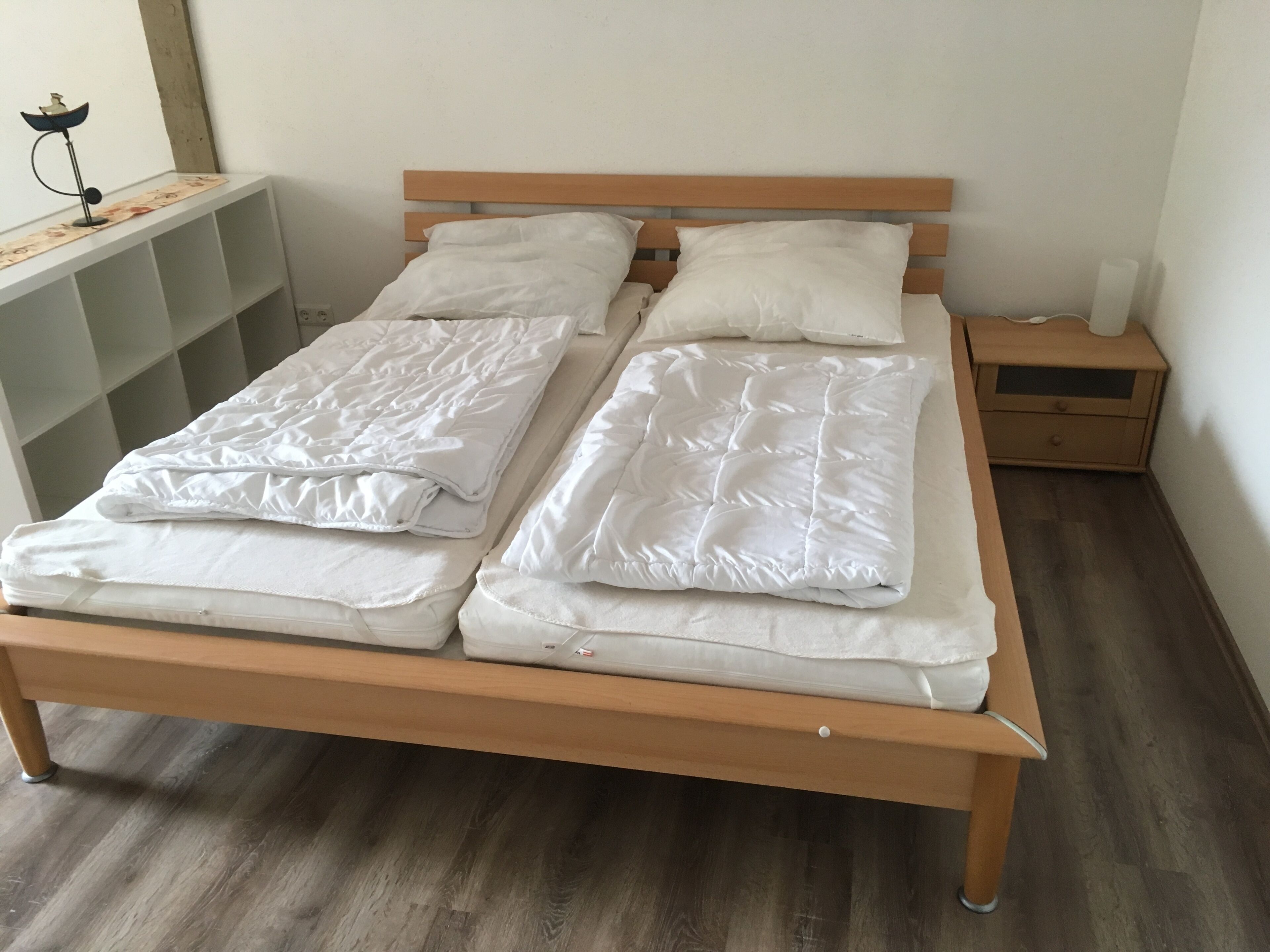A double bed with a wooden frame and white bedding, a bedside table with a lamp, and a nightstand with a lamp.