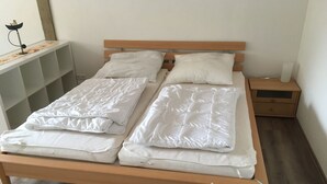 A double bed with a wooden frame and white bedding, a bedside table with a lamp, and a nightstand with a lamp. - Holidays with pony rides, WiFi, TV, dishwasher, oven (Butjadingen - Stollhamm)