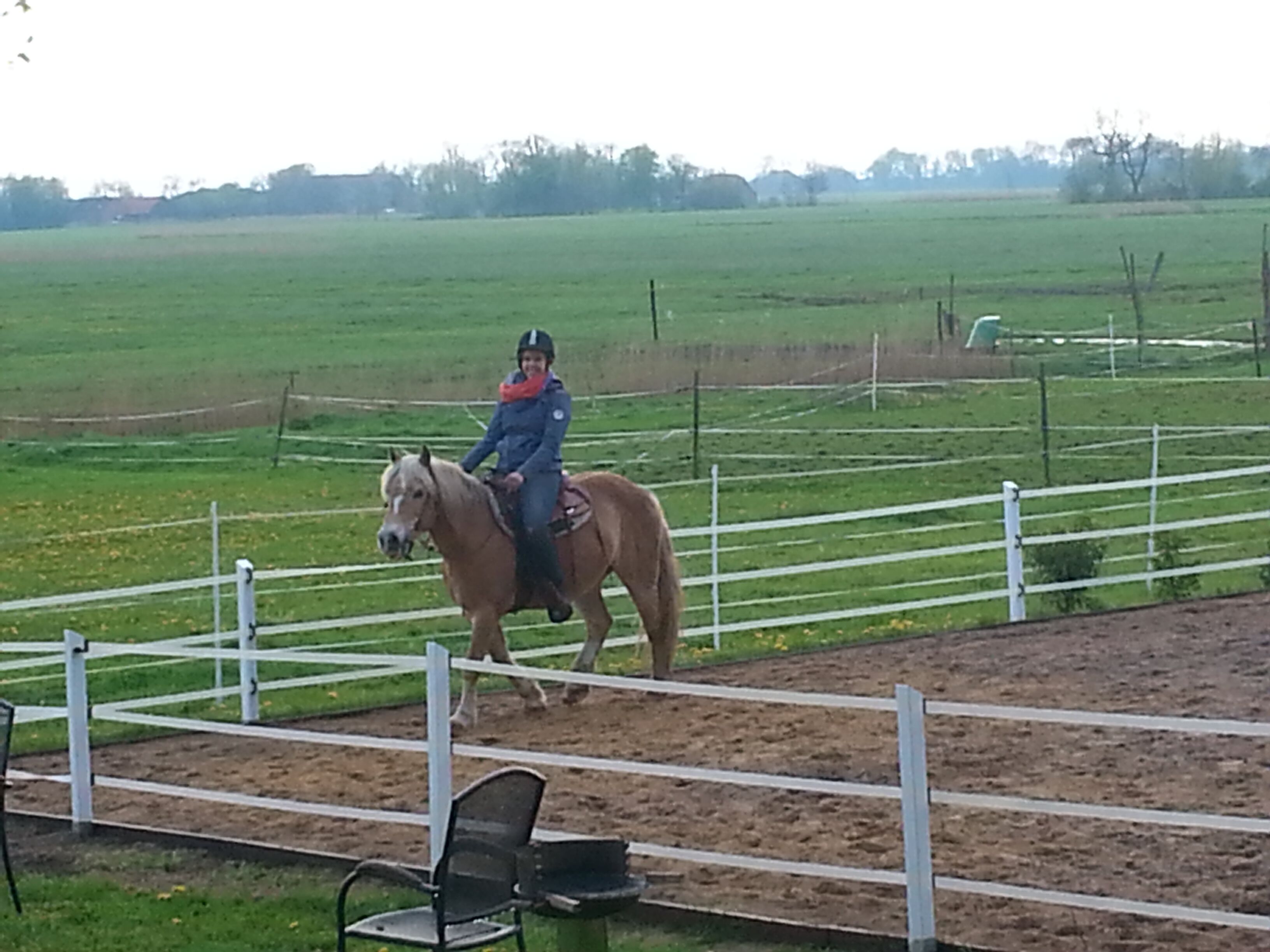 Une personne à cheval dans une arène en plein air, entourée d’une clôture blanche.