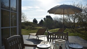 An outdoor wooden deck with a table set for two, a wooden chair, and a large umbrella. - Large, detached cottage, 5 stars, near the beach, beautiful view. (Buren)