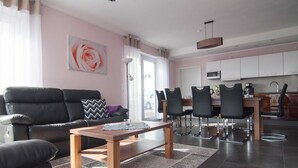 A modern living room with a black leather sofa, a wooden coffee table, and a dining area with a kitchen in the background. - Ambience apartment with terrace - modern-one | Attractive apartment w. (Fulda)