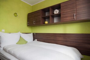 A bed with white bedding, a green wall, and wooden cabinets above it.