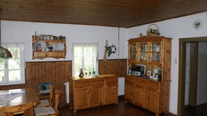 Une pièce aux murs lambrés, comprenant une table à manger, des chaises, un buffet aux portes vitrées et une fenêtre avec des rideaux.