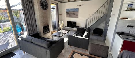 Una sala de estar moderna con chimenea, sofás grises, una mesa de centro y una escalera que sube a otro nivel.