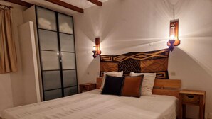 Un dormitorio con una cama grande, cabecera de madera, dos mesitas de noche, una lámpara de pared y una puerta corrediza de vidrio.