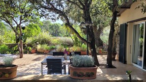 An outdoor patio area with a table and chairs, surrounded by potted plants and trees.