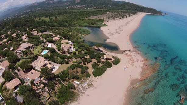 Vista aérea de una zona costera con playa, aguas cristalinas y una área residencial con casas y vegetación.