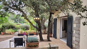 Un patio al aire libre con mesa y sillas, rodeado de plantas en macetas y árboles.