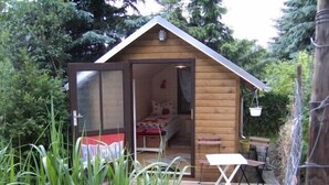 Una pequeña cabaña de madera con la puerta abierta, mostrando una cama y una mesa.