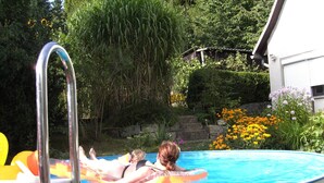 Una piscina con dos personas en flotadores, rodeada de abundante follaje y flores.