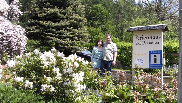 Señal que indica un espacio para 2 a 5 personas, probablemente un alojamiento pequeño o casa de huéspedes, rodeado de exuberante vegetación y plantas en flor.