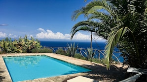 En pool med kristallklart blått vatten, omgiven av stengolv, med en fantastisk utsikt över havet.