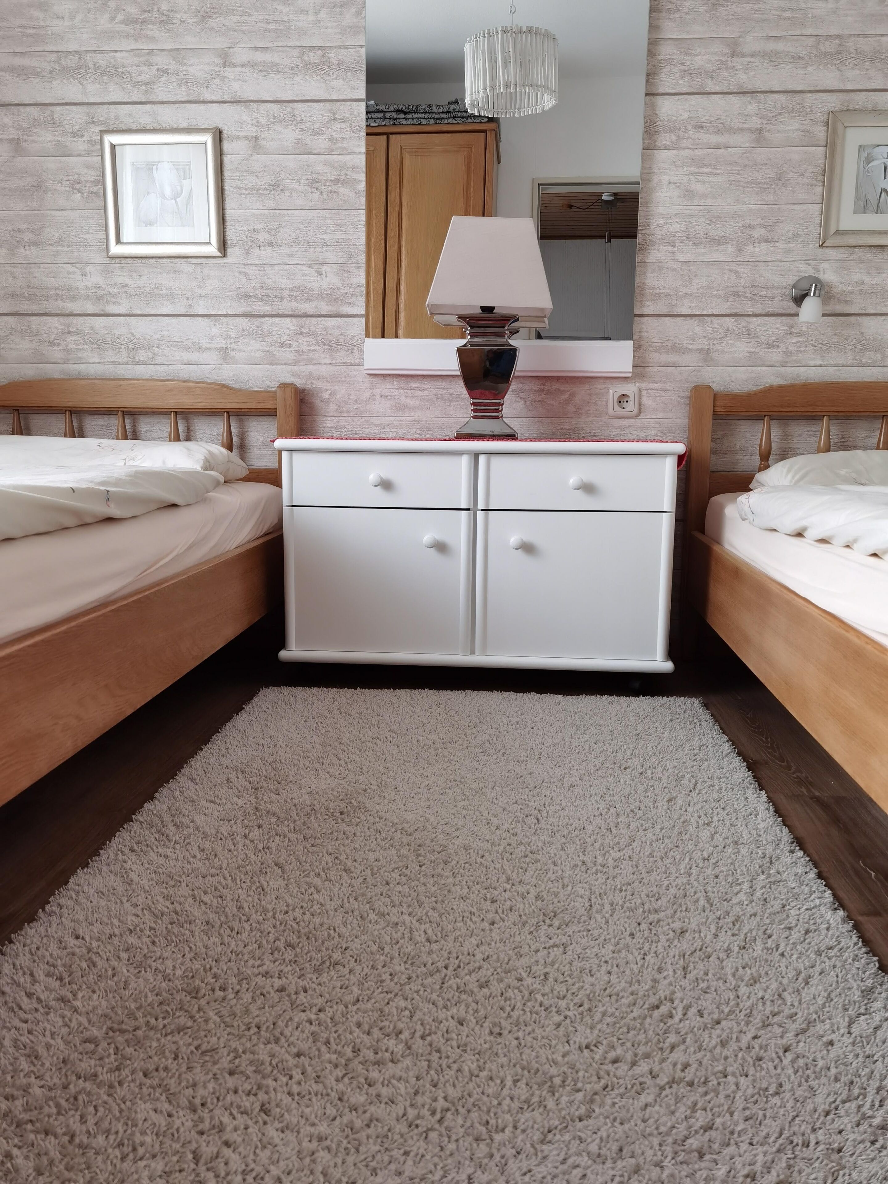 Une chambre avec deux lits, une commode, un miroir et un lustre.