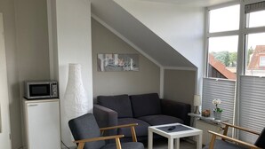 A modern living room with a sofa, two armchairs, a coffee table, a small cabinet with a microwave, and a large window with blinds. - Top apartment with 2 bedrooms, balcony and internet flat rate (Grömitz)