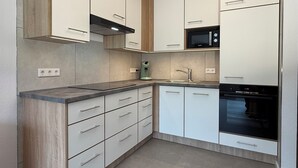 A modern kitchen with white cabinets, a black microwave, and a built-in oven. - Seeschlößchen Thatched Cottage, "Westmöwe" Vacation Rental, just 200 meters from the beach (Büsumer Deichhausen)