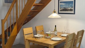 A dining area with a wooden table set for four, surrounded by wooden chairs. A wooden staircase is visible to the left. - Seeschlößchen Thatched Cottage, "Westmöwe" Vacation Rental, just 200 meters from the beach (Büsumer Deichhausen)