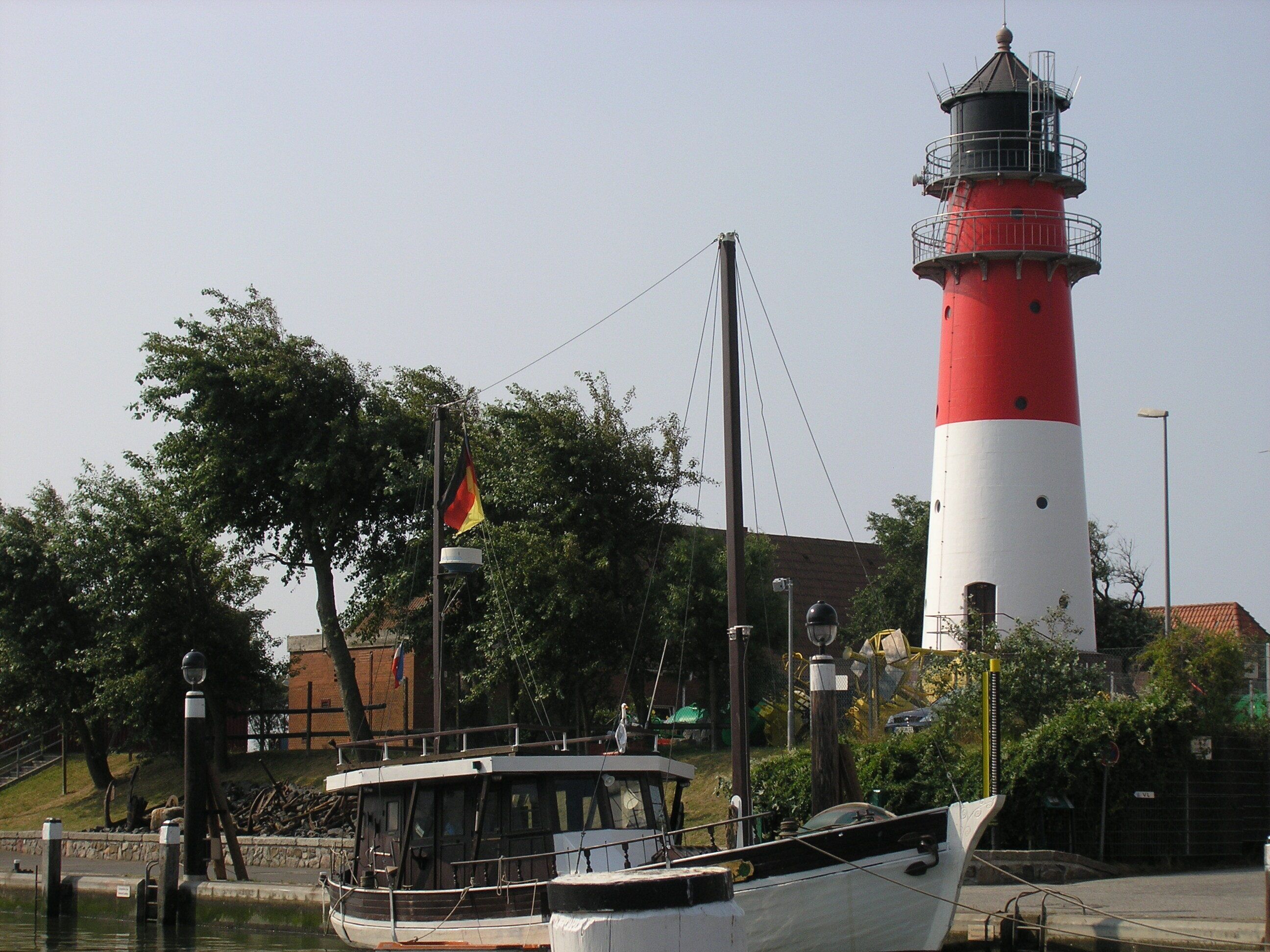 A lighthouse with a red and white exterior, a boat docked nearby, and a flagpole with a flag.