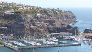 Un puerto costero con barcos amarrados, rodeado de acantilados rocosos y edificios residenciales.