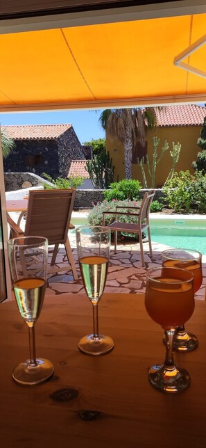 Ein Tisch mit drei Gläsern Getränken, ein Holzstuhl und Blick auf einen Pool und Gebäude.