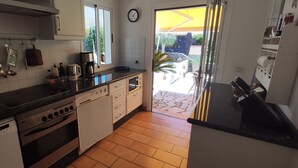 Cocina con armarios blancos, encimera negra y piso de baldosas. Se ve un jardín a través de la ventana.