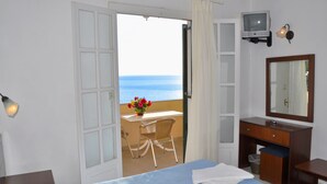 Habitación de hotel con cama, escritorio con silla, televisor y balcón con vista al mar.