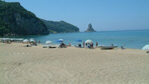 Una playa con sombrillas y sillas reclinables, un bote y un acantilado rocoso al fondo.