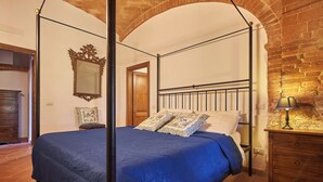 A bedroom with a four-poster bed, a wooden dresser, and a mirror on the wall. - Apartment with a beautiful covered terrace in front of the pool (Torrita di Siena)