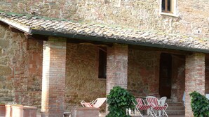 A rustic stone building with a tiled roof, outdoor seating area with chairs, and a small garden. - Apartment with a beautiful covered terrace in front of the pool (Torrita di Siena)