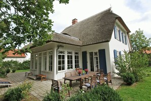 A white house with a thatched roof, a covered patio with wooden furniture, and a garden. - Traditional thatched house 11.09. to 11.10. 25 15 % discount please ask for price (Ostseebad Prerow)