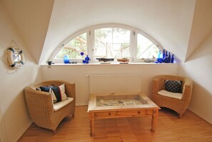A cozy attic room with a sloped ceiling, two wicker chairs, a wooden table, and a large window with nautical decorations. - Traditional thatched house 11.09. to 11.10. 25 15 % discount please ask for price (Ostseebad Prerow)