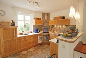 A kitchen with wooden cabinets, a tiled backsplash, a stove, and a fruit bowl on the counter. - Traditional thatched house 11.09. to 11.10. 25 15 % discount please ask for price (Ostseebad Prerow)