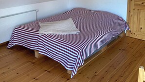 Une petite chambre avec un lit simple, un plafond en pente et des poutres en bois.