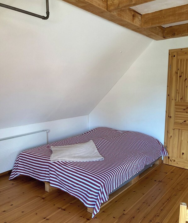 A small, single-bed room with a sloped ceiling and wooden beams.