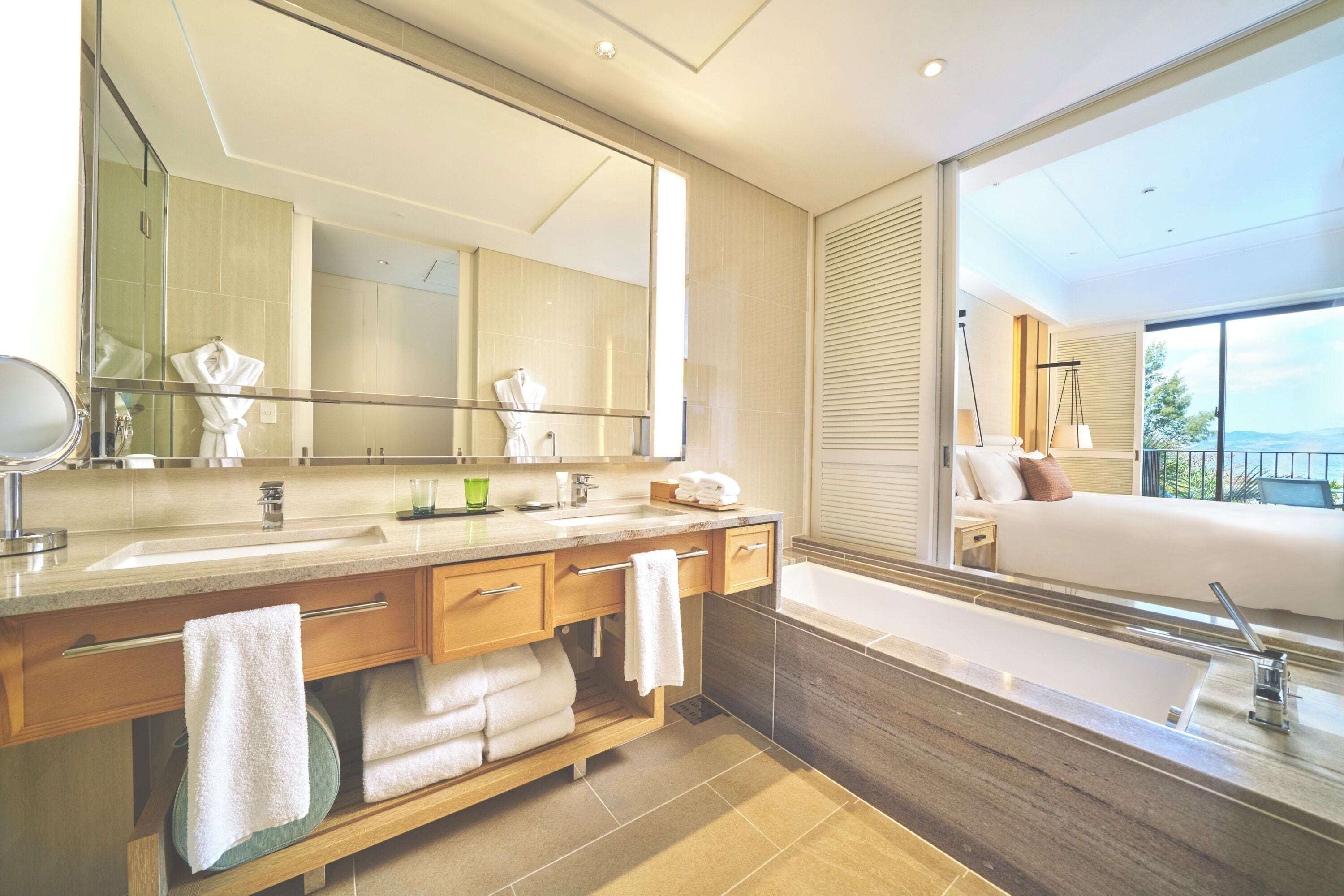 A modern bathroom with a large mirror, a bathtub, and a sink. There are towels and toiletries on the counter.