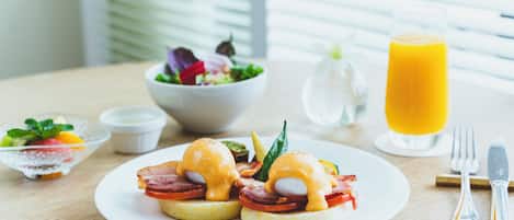 A breakfast setting with eggs benedict, a glass of orange juice, and a bowl of salad on a wooden table.