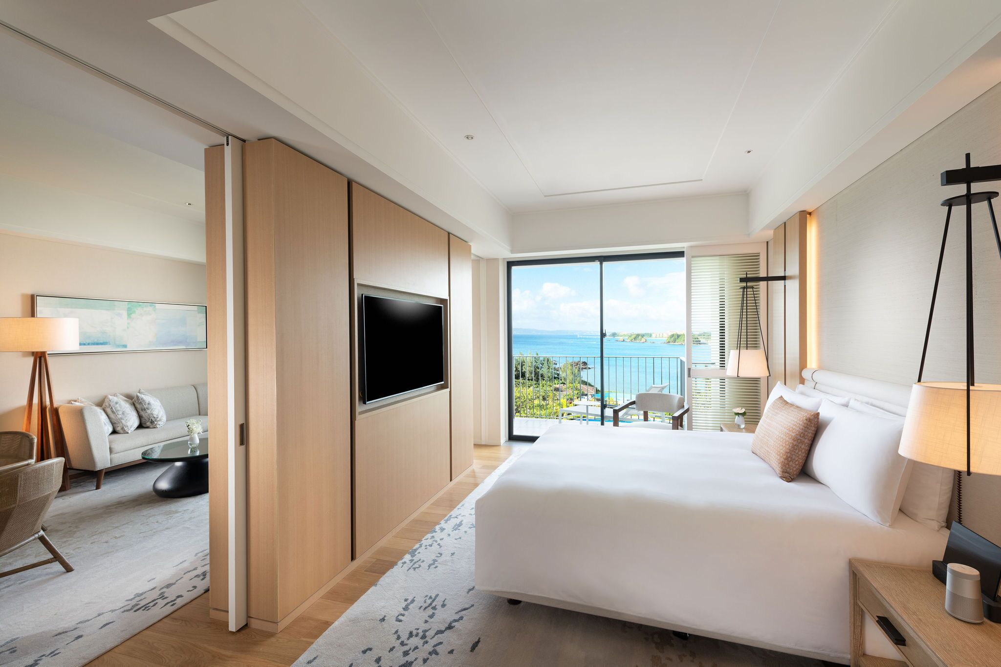 Una habitación de hotel moderna con una cama grande, un televisor de pantalla plana, un balcón con vistas al mar y una zona de sofás.