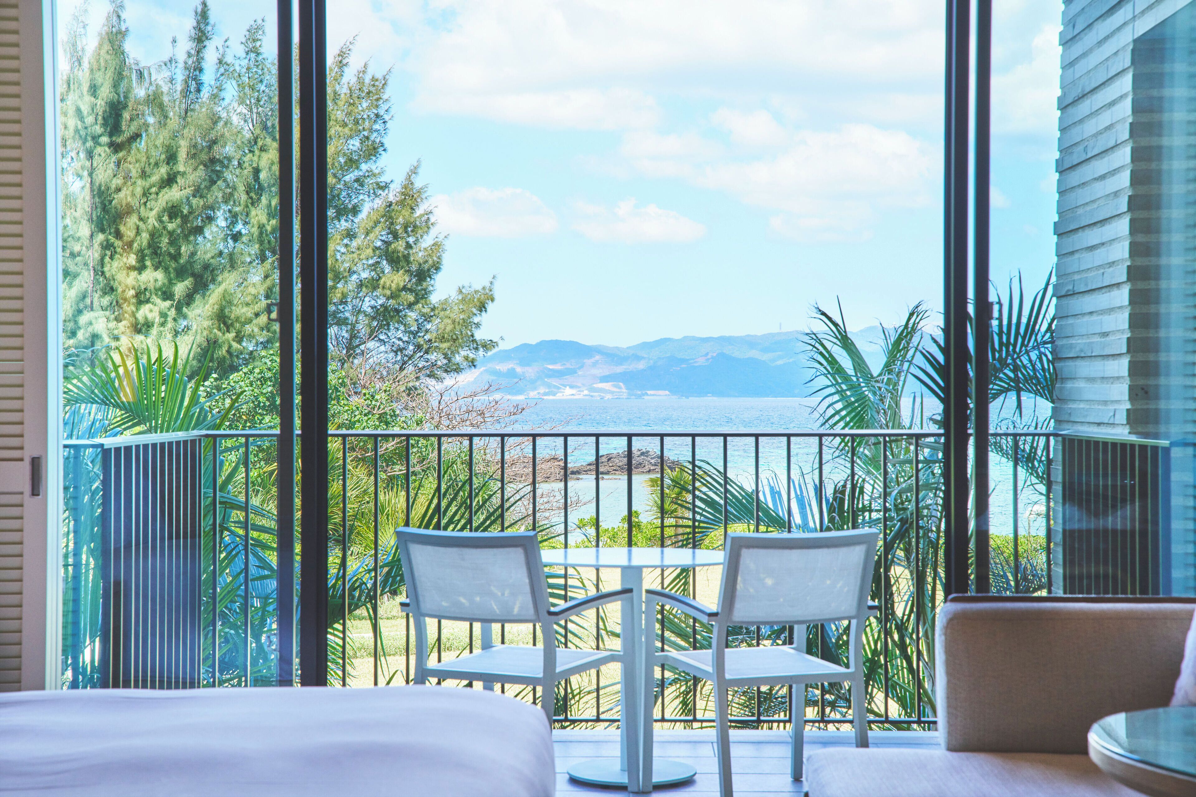 A balcony with a view of the sea, two chairs, and a table.