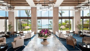 Un'ampia hall con un'elegante composizione floreale al centro, arredi moderni e grandi finestre che offrono vista sull'oceano.