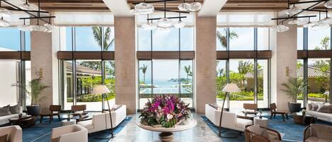A spacious lobby with a central floral arrangement, modern furniture, and large windows offering a view of the ocean.