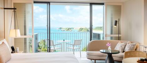 Habitación de hotel con una cama grande, un sofá, una mesita y un balcón con vista al mar.