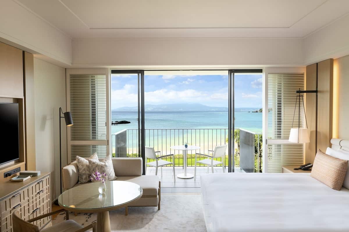 A hotel room with a balcony, a bed, a TV, a desk, and a chair.